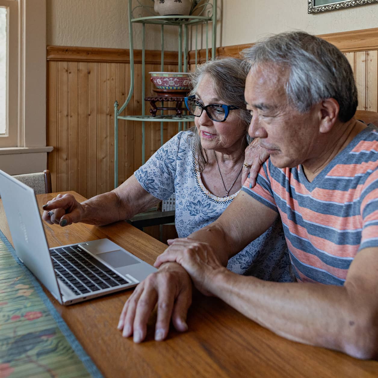 An older couple discussing something on their laptop screen.