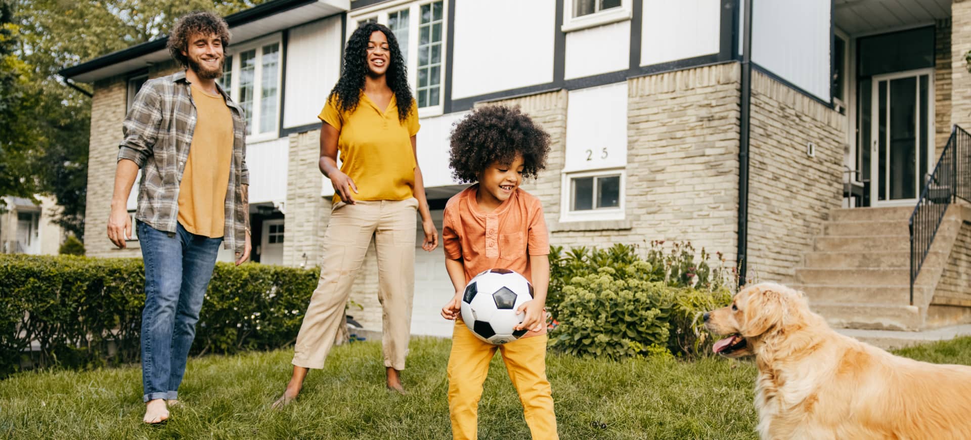 A family playing with a soccer ball in the yard with their dog.