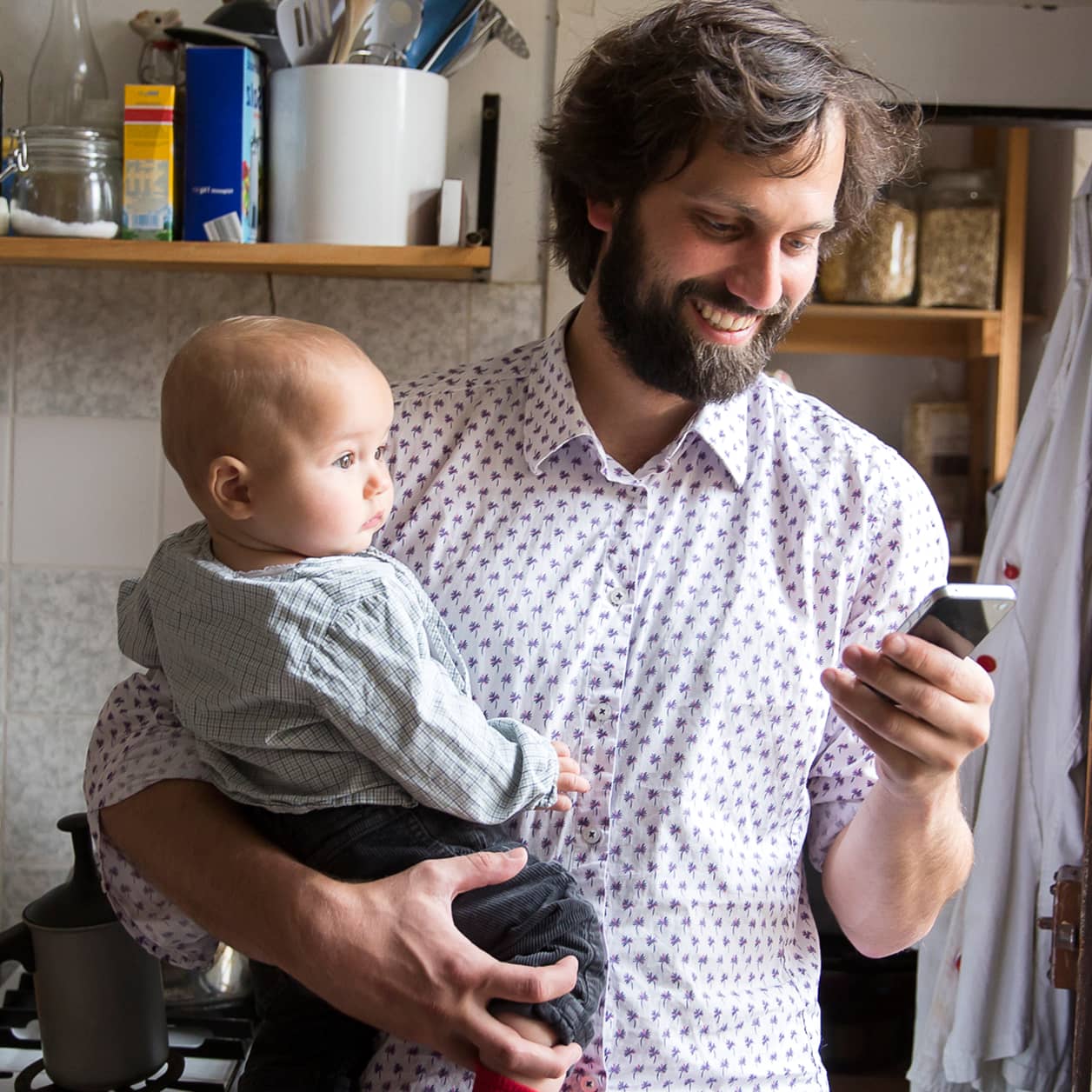 A parent holding their baby and looking at the cell phone in their other hand.