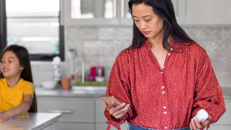 A person in their kitchen checking a prescription on their cell phone.