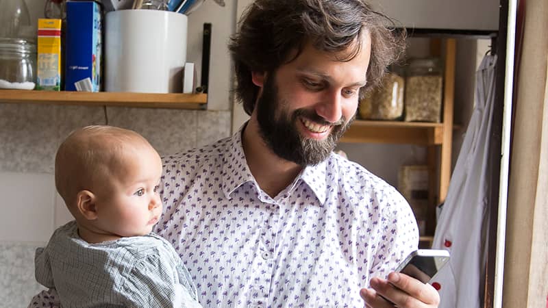 A parent holding their baby and looking at the cell phone in their other hand.