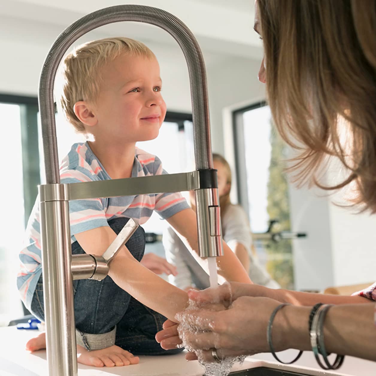 A parent washing their hands while a child watches.