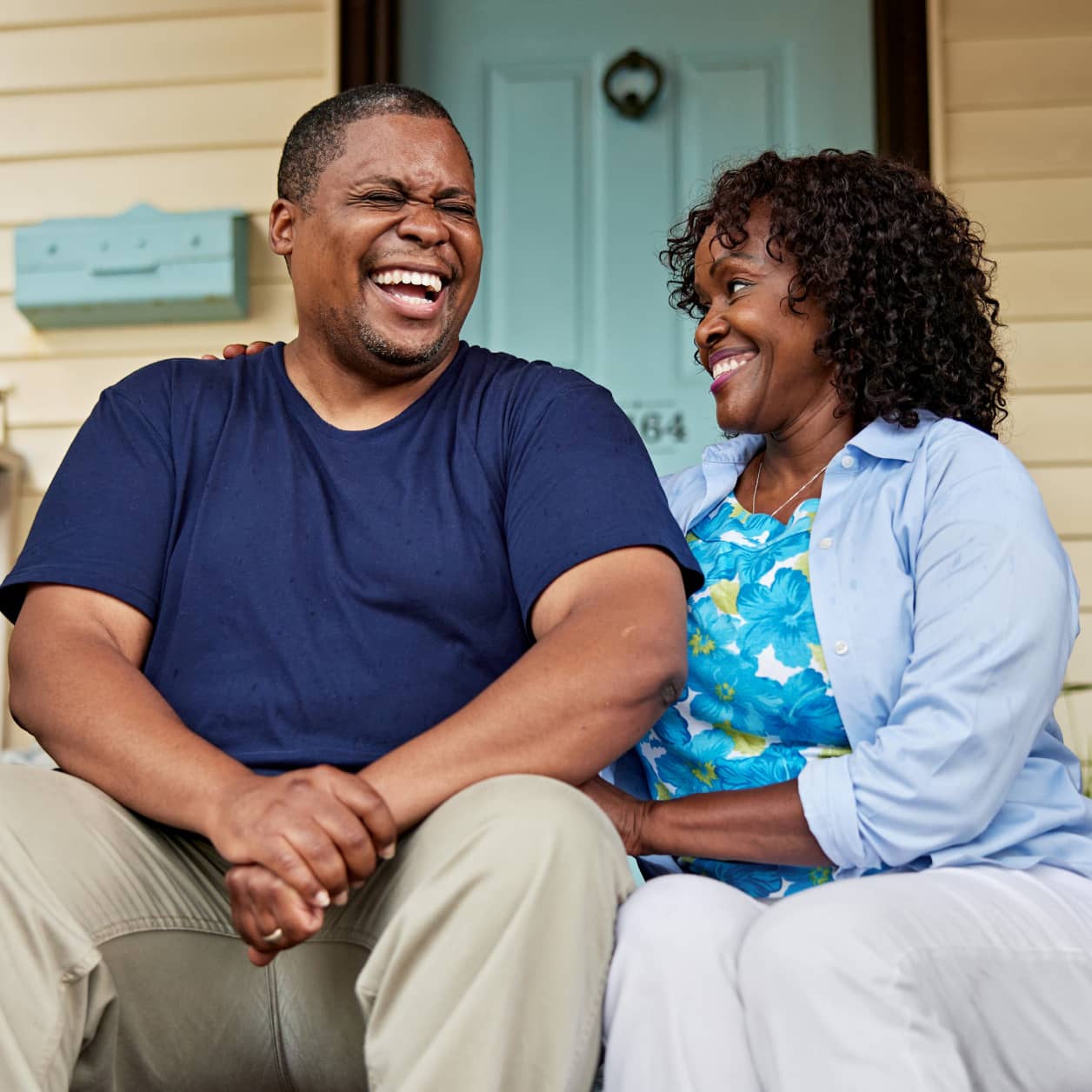 A couple laughing while waiting for a delivery on their front steps.