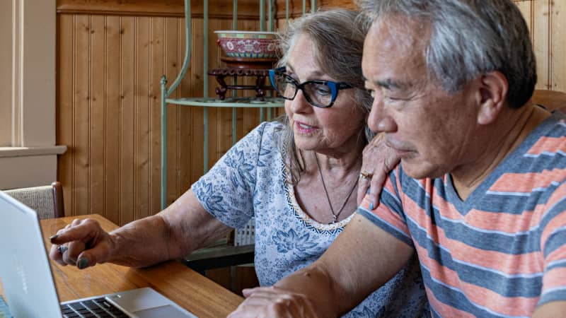 An older couple discussing something on their laptop screen.