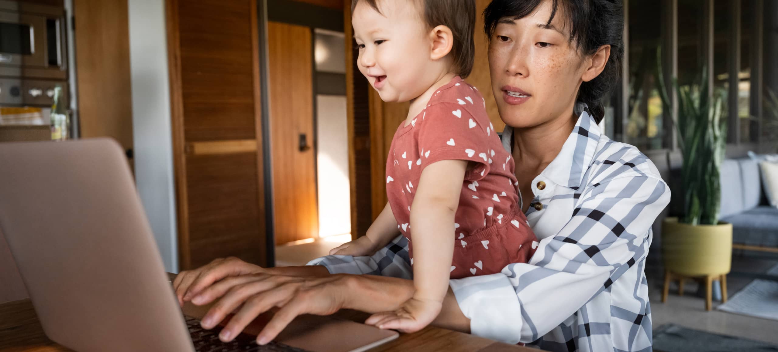 A young child on their parent's lap while the parent types on a laptop.