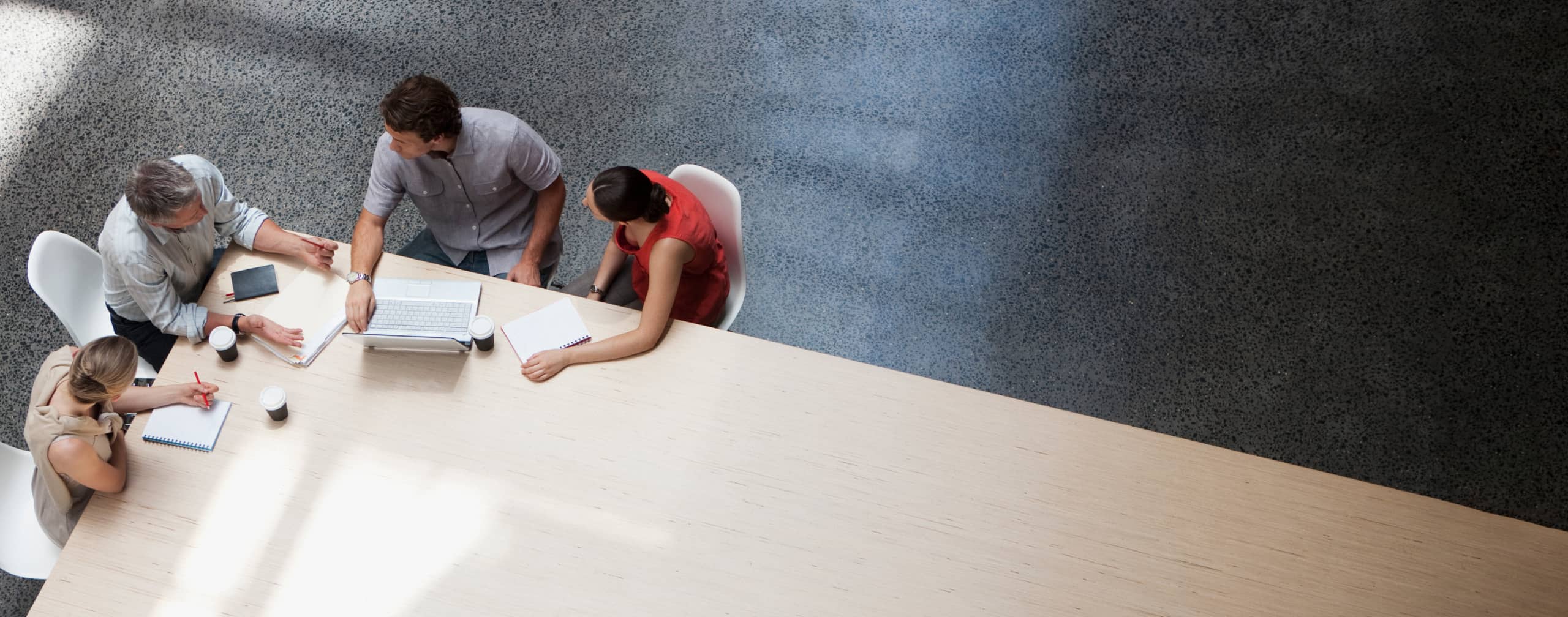 Four colleagues working together at one end of a conference table seen from above.