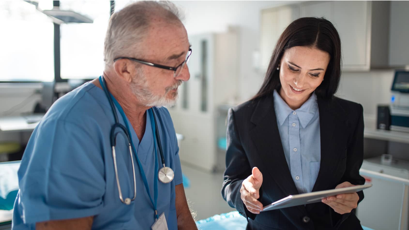 Healthcare professional and businessperson discussing information on a digital tablet in a clinical setting
