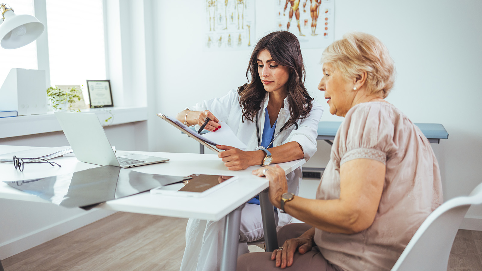 Healthcare professional showing notes to a seated patient at a desk.