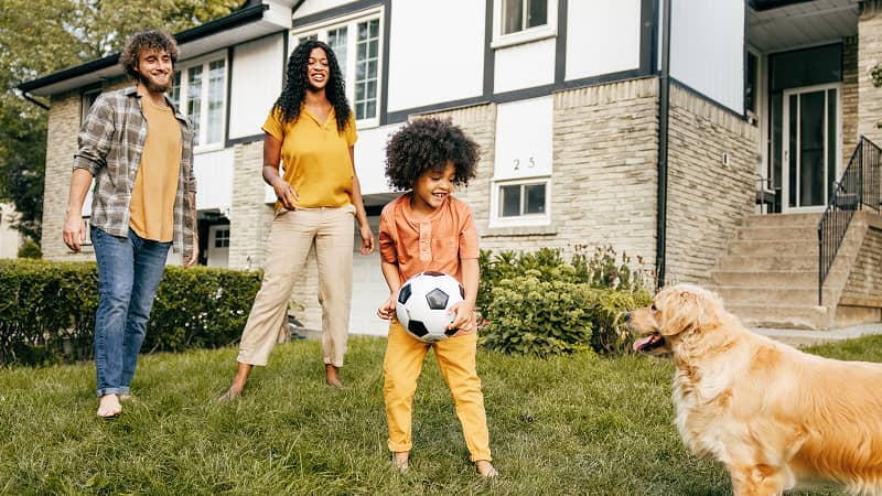 Parents and a child play in the yard with a soccer ball and their dog