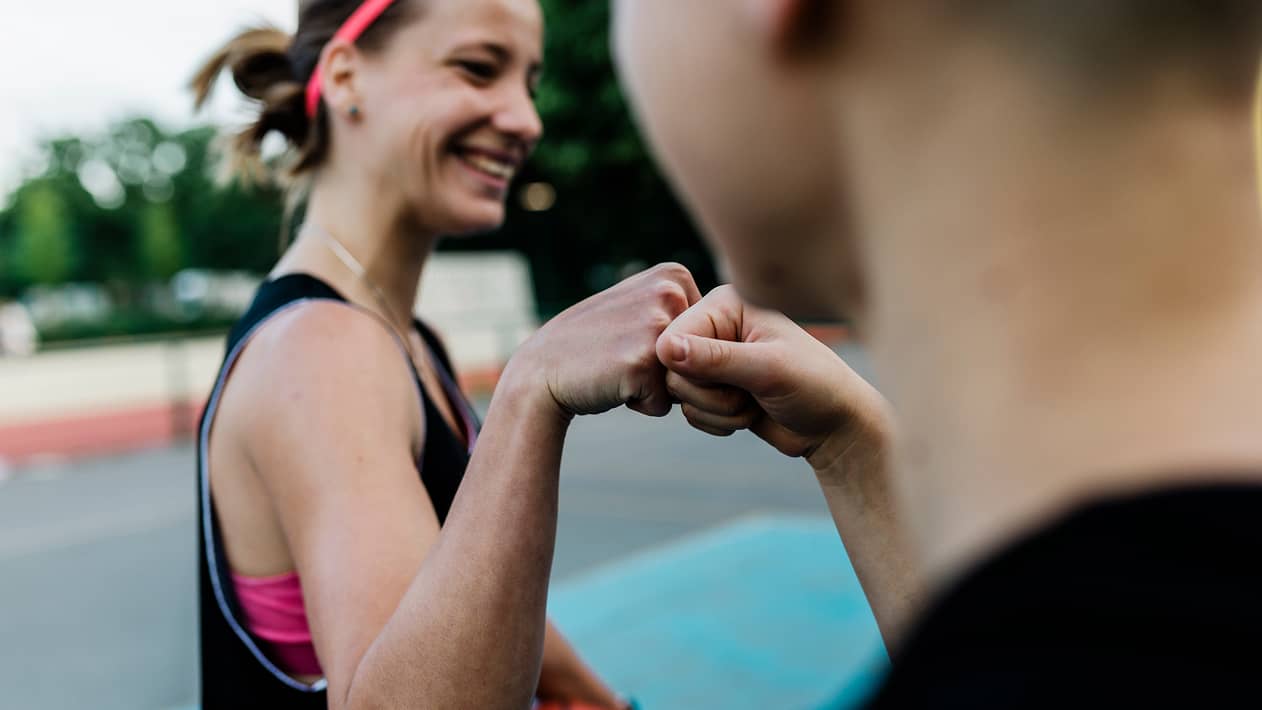 Two people fist bumping outside on a sports court