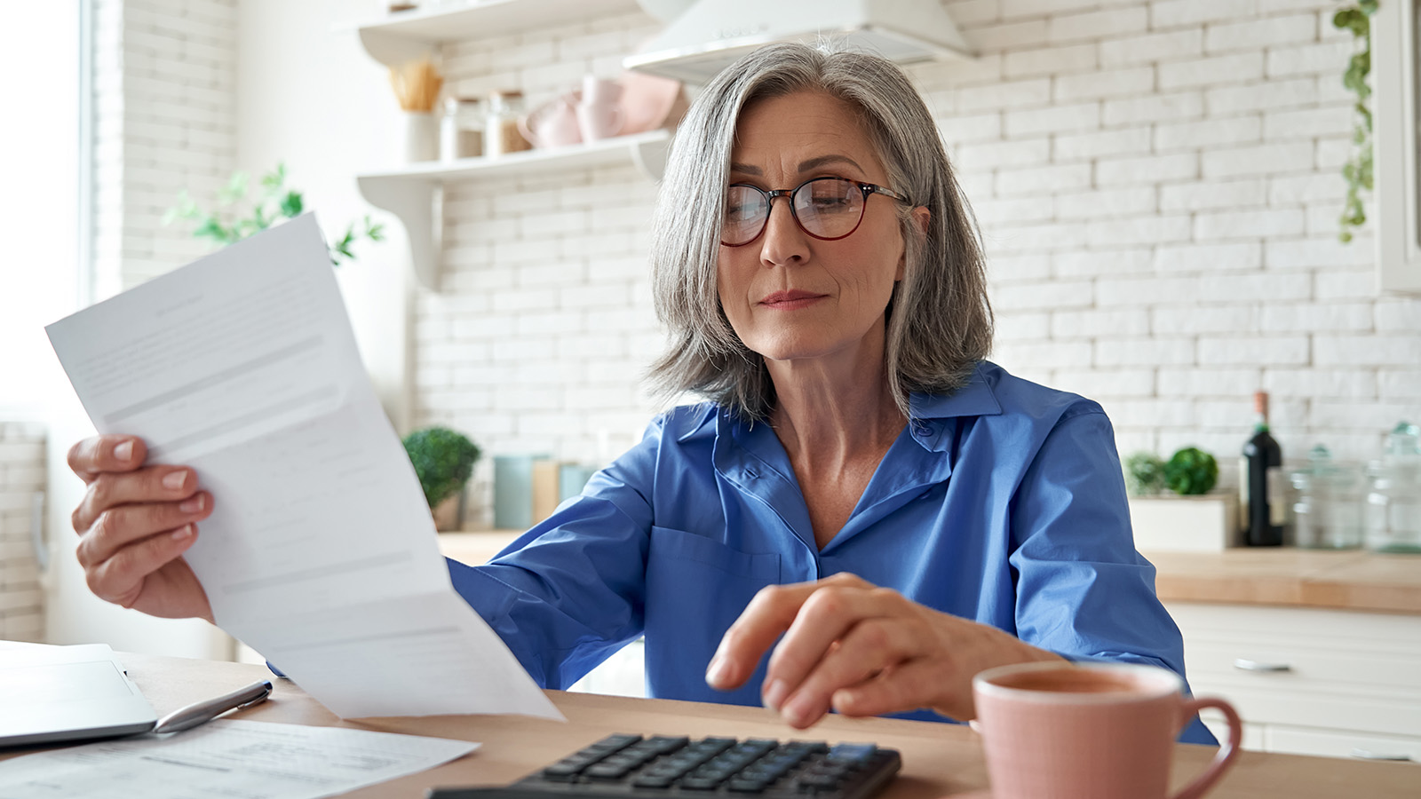 Person reviewing documents while sitting at a kitchen table with a calculator.