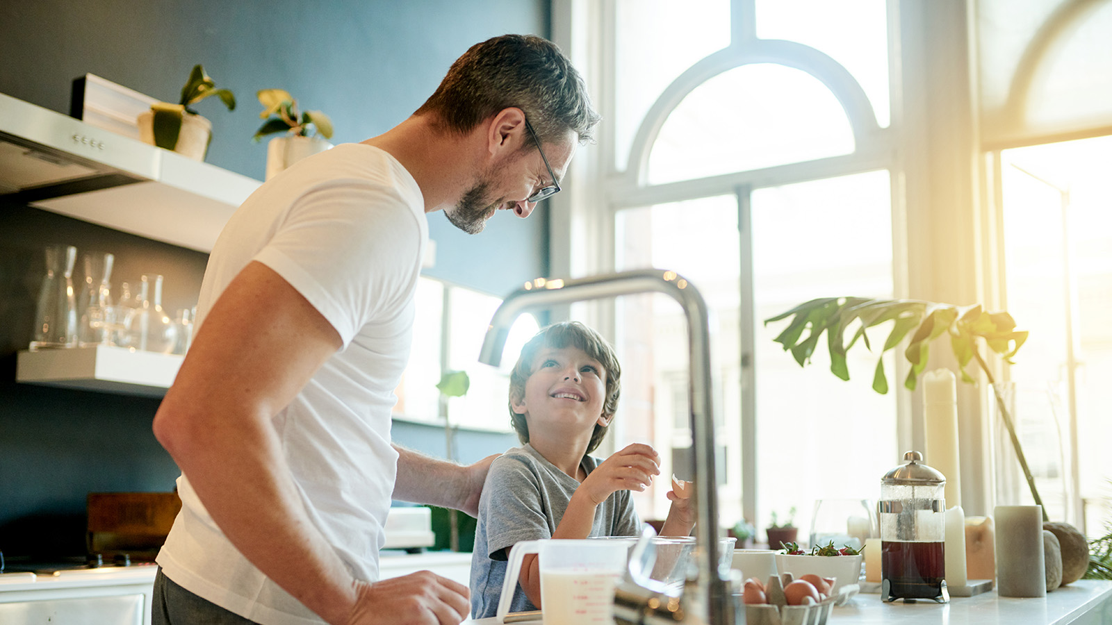Parent and child cooking together in a sunny kitchen.