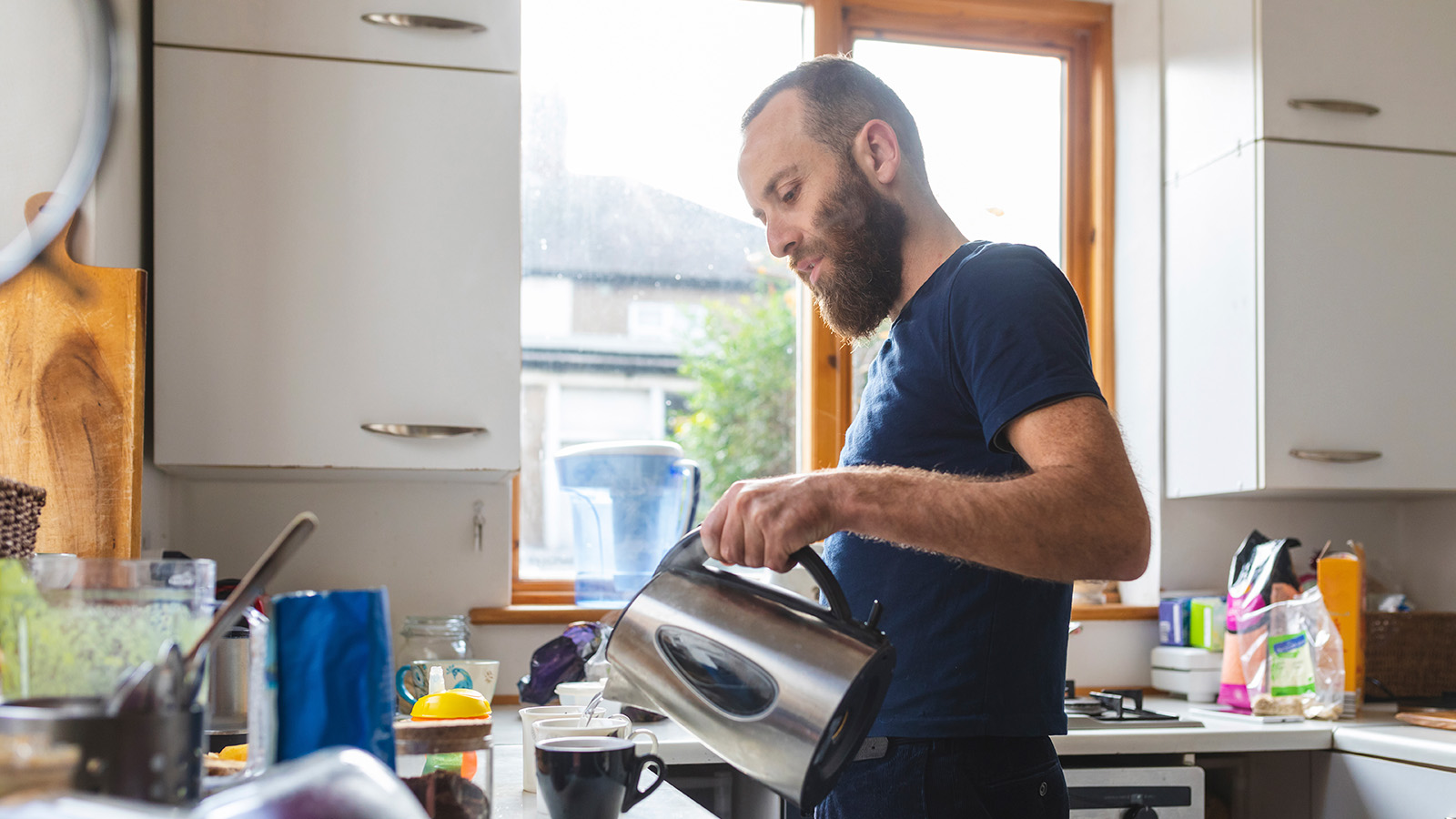 Man pouring water into a cup while standing in a kitchen.