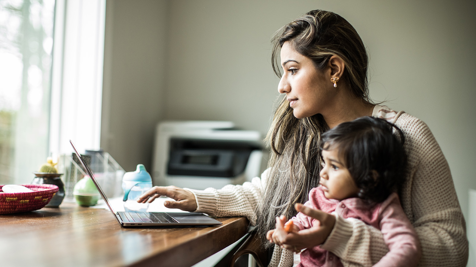 A woman using a laptop while holding a child.