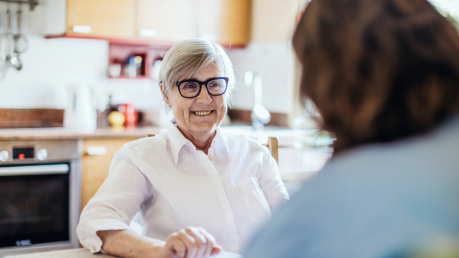 An older person sitting at a table, engaged in conversation.