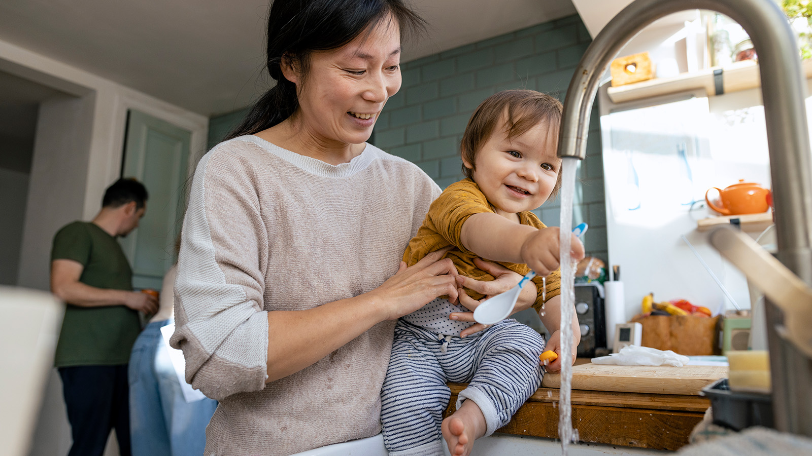 Adult and child playing with water at a kitchen sink.