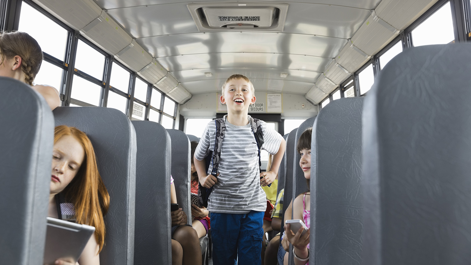 Child standing on a school bus surrounded by classmates.