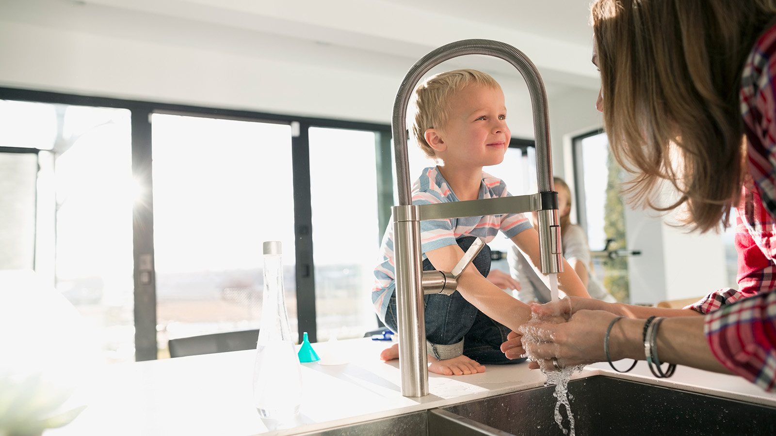 Adult helping a child wash hands at a kitchen sink.