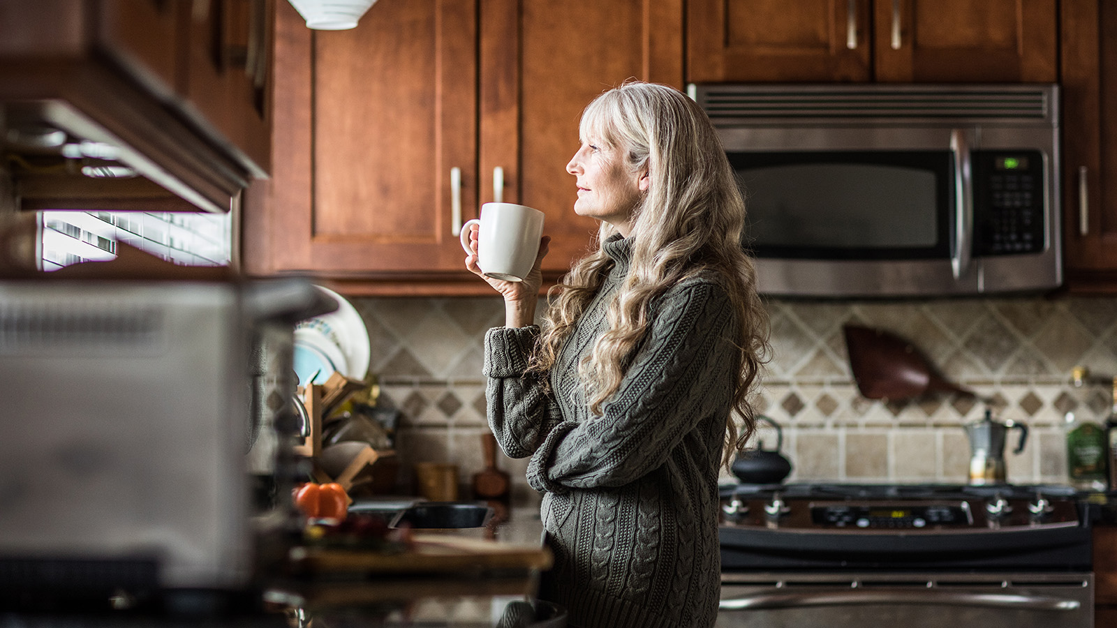 Woman holding a coffee cup while standing in the kitchen.