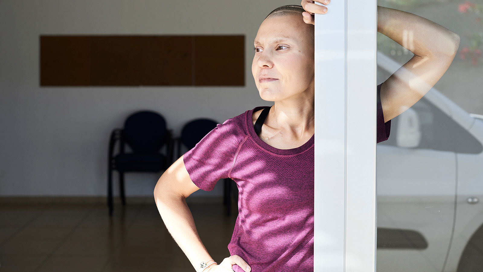 A woman leans against a doorframe, wearing athletic clothing, with a relaxed posture in a bright, open space.