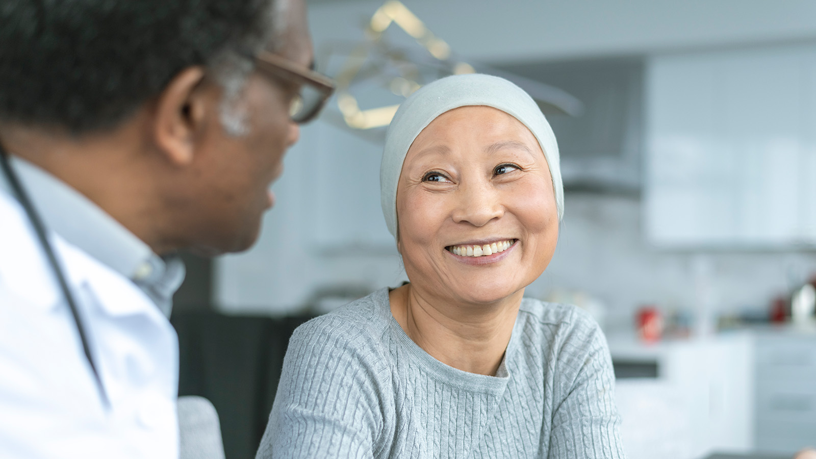 A healthcare professional listens attentively to a patient, who is wearing a light gray sweater, in a modern setting.