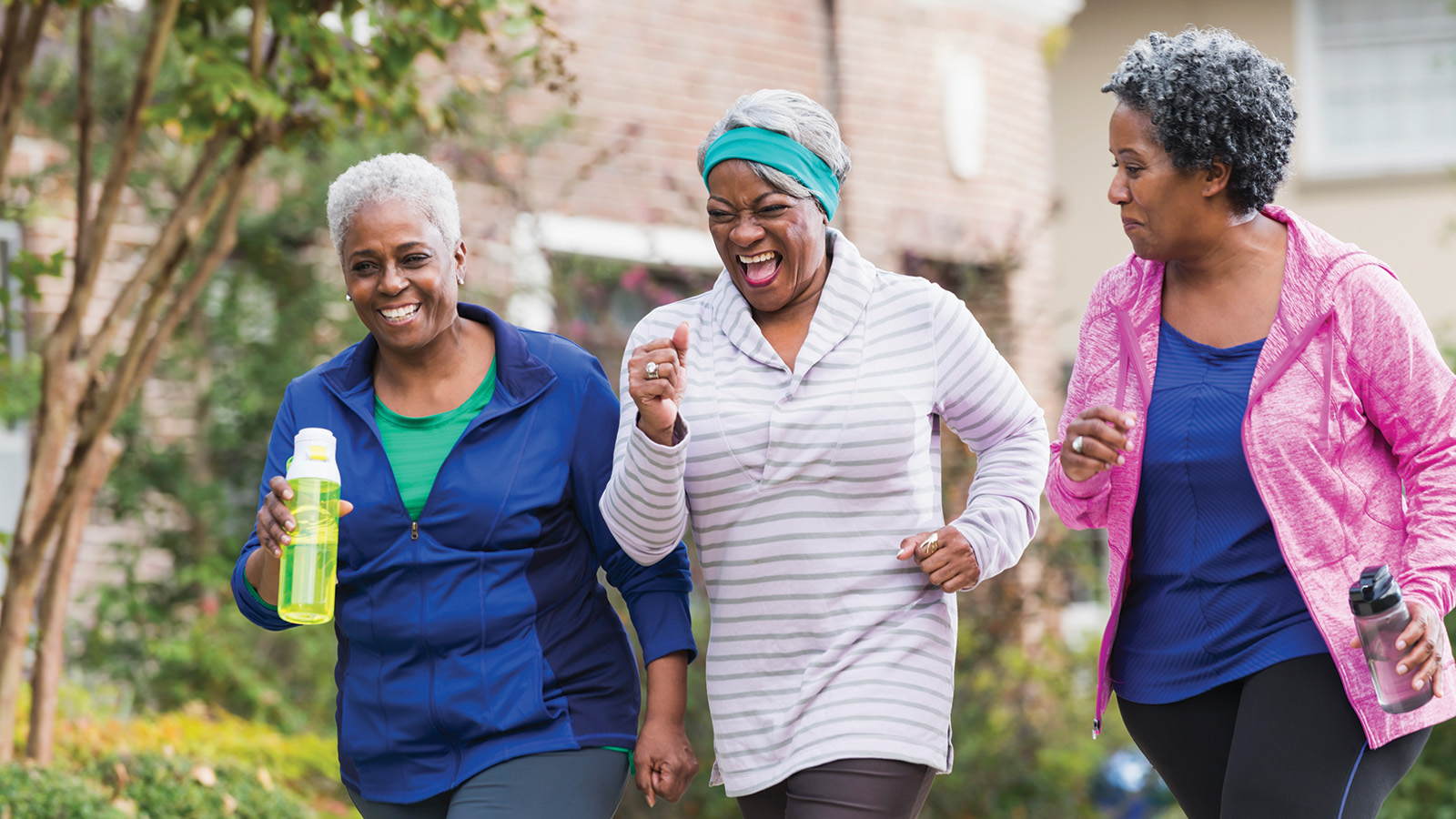 Three older women jog together outdoors, one holding a water bottle, enjoying their exercise in a neighborhood setting.