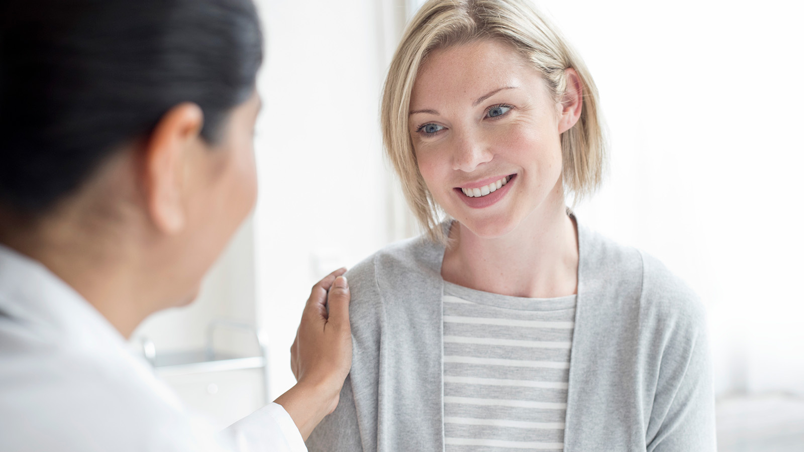 A healthcare professional comforts a patient during a consultation in a bright, modern office setting.