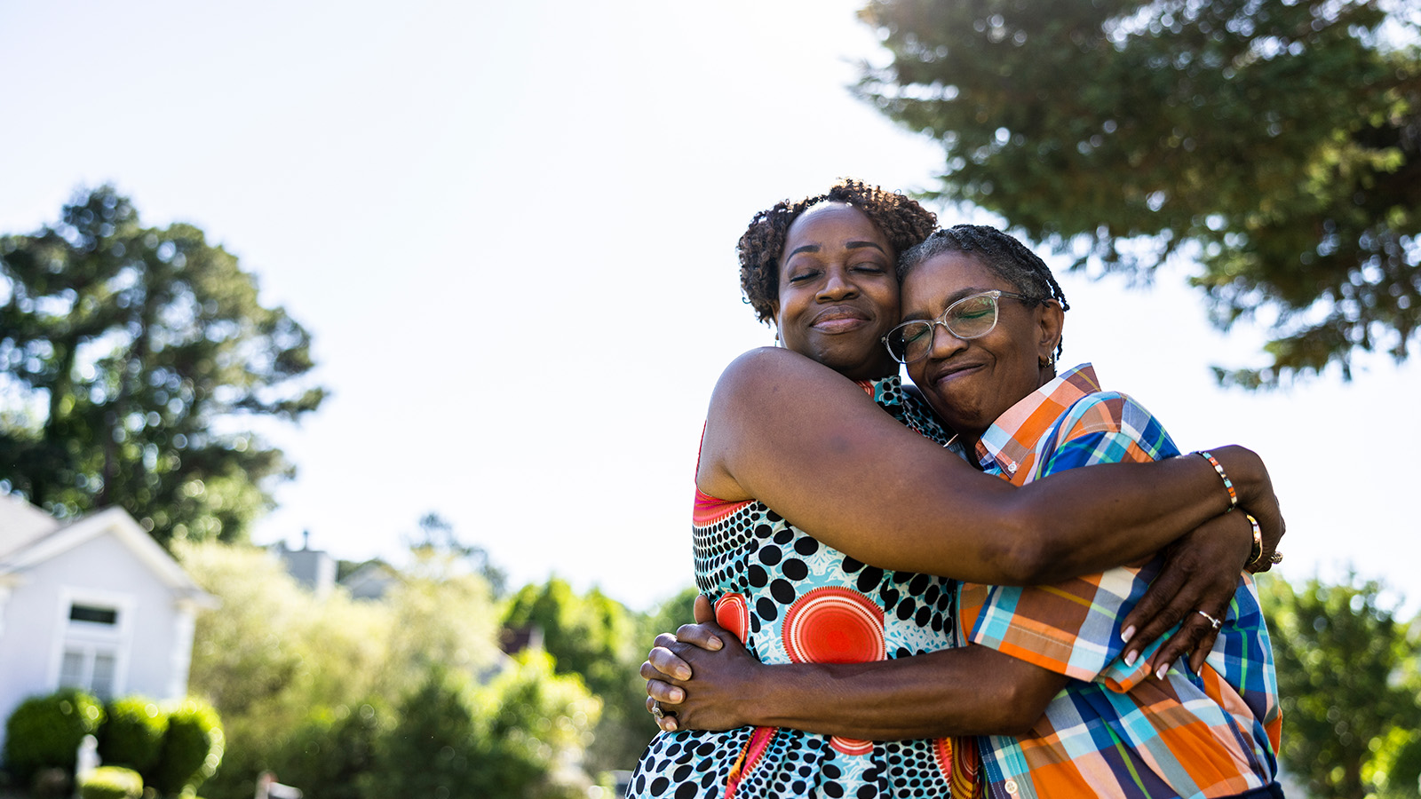 Two people embrace outdoors, surrounded by trees and sunlight, conveying warmth and affection in a joyful moment.