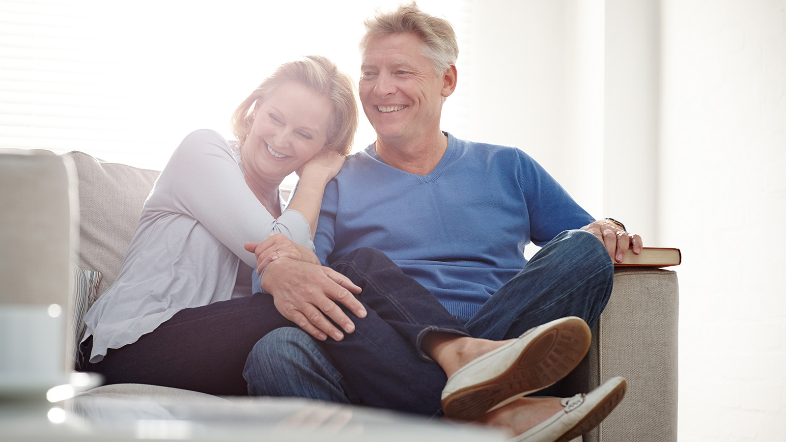 A couple sits closely together on a couch, sharing a moment of intimacy and comfort in a cozy living room.