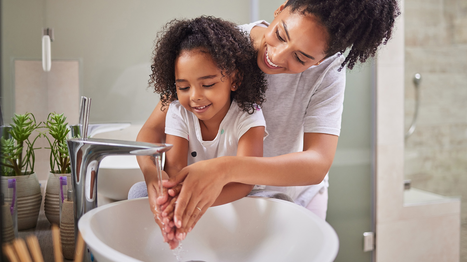 A parent and child wash their hands together at a bathroom sink, promoting hygiene in a bright, clean space.