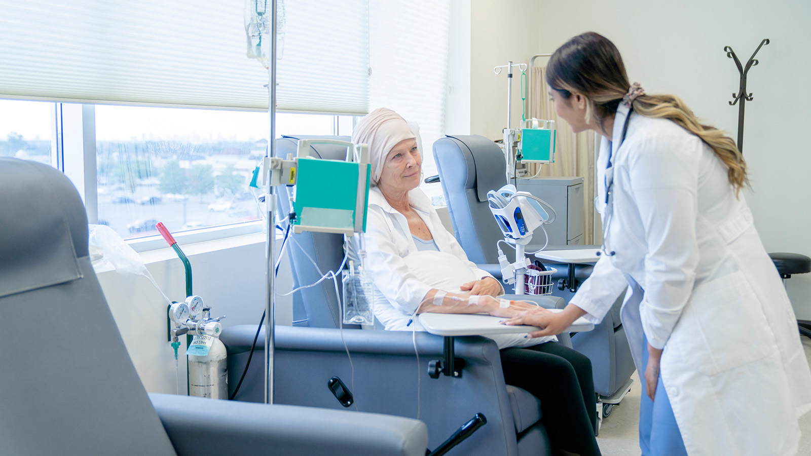 A patient receiving treatment in a medical chair, with an IV drip and a healthcare professional attending to them.