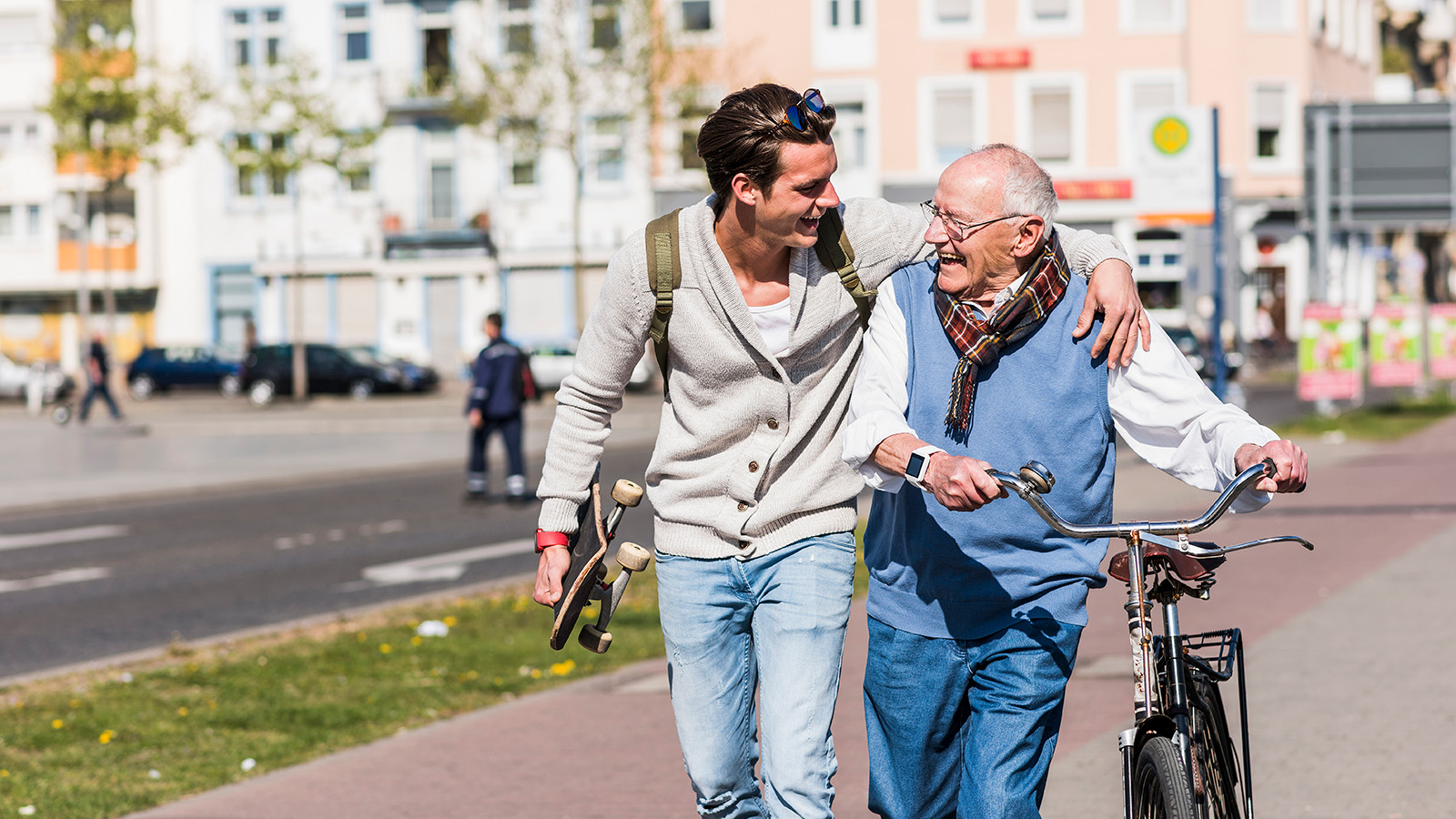 A young man assists an elderly man walking with a bicycle on the street