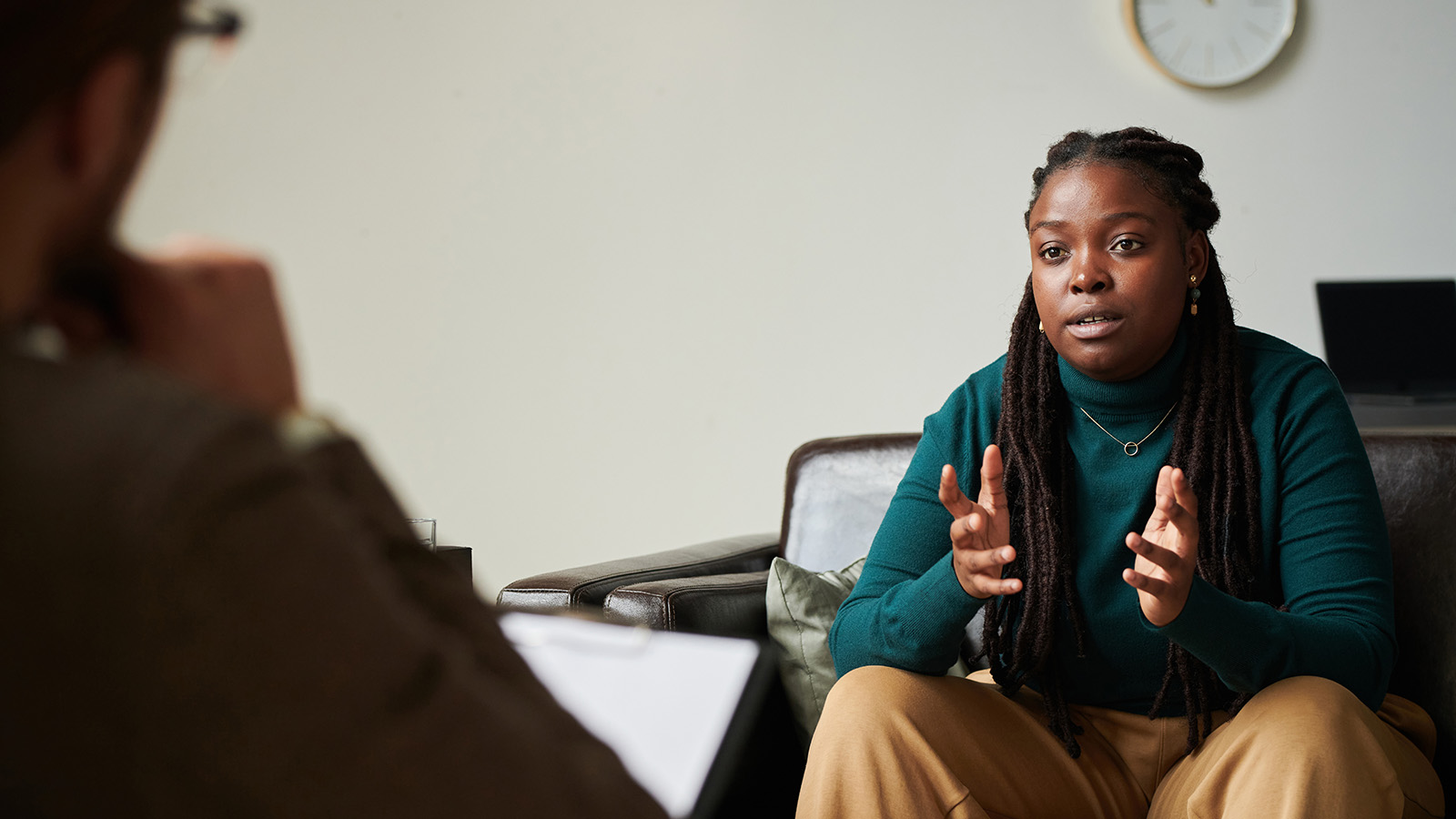 A woman gestures while speaking to a therapist, sitting on a couch in a cozy office.