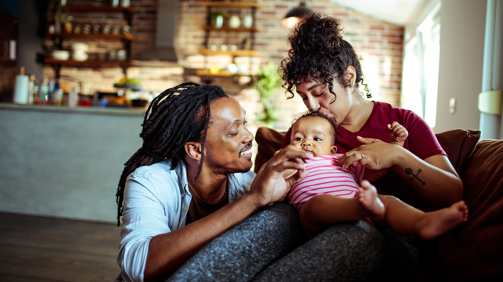 A family sits on a couch, engaging with a baby, with parents interacting and sharing a joyful moment together.
