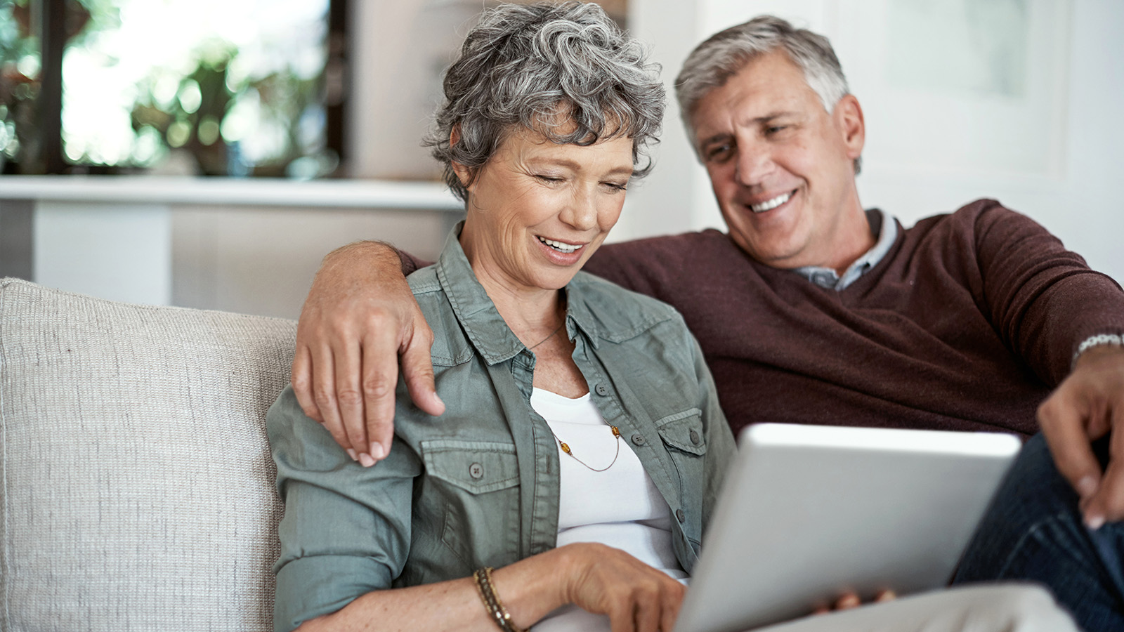 An older couple sits together on a couch, looking at a tablet.
