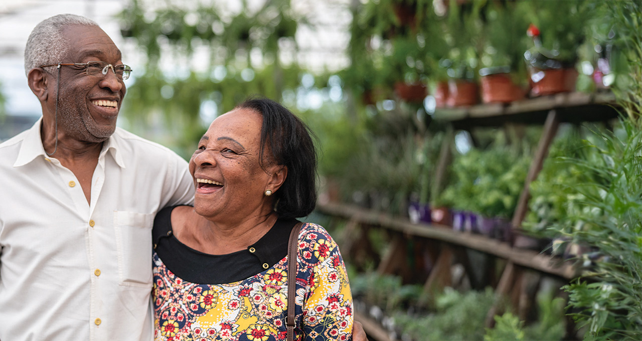 An elderly couple posing together in a greenhouse