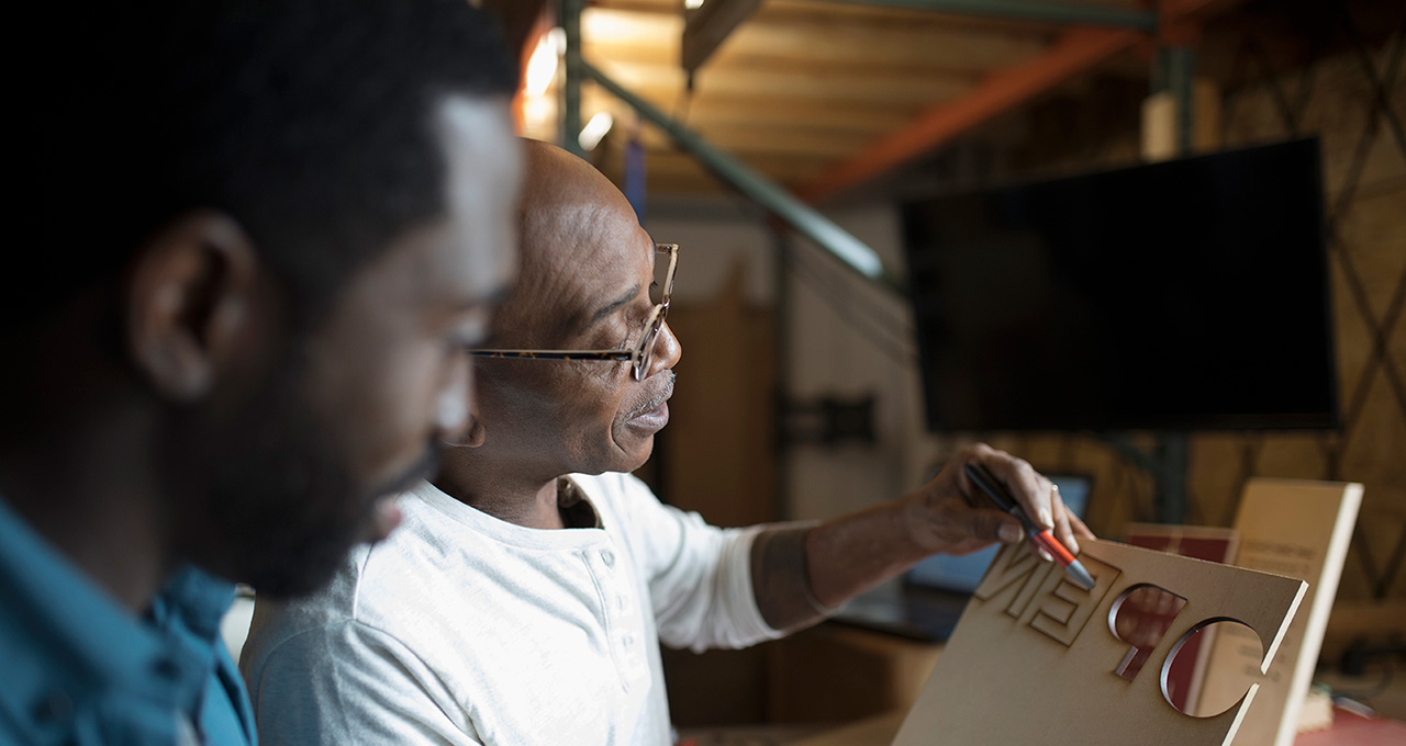 Two individuals discussing a wooden sign in a workshop