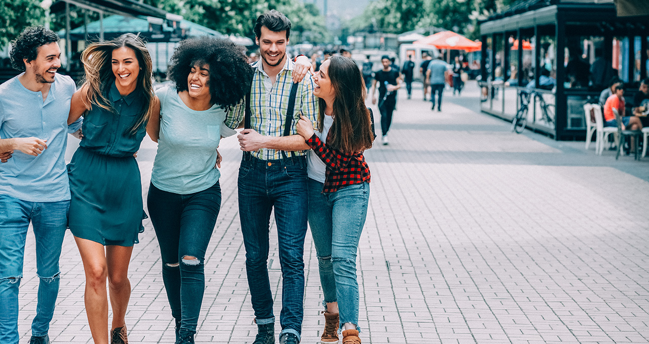 A group of friends walks closely together on a bustling street, enjoying each other’s company and the vibrant atmosphere.