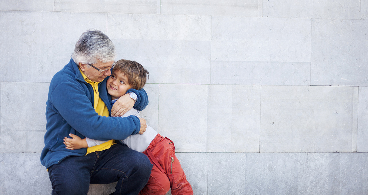 An elderly man hugging a child against a stone wall