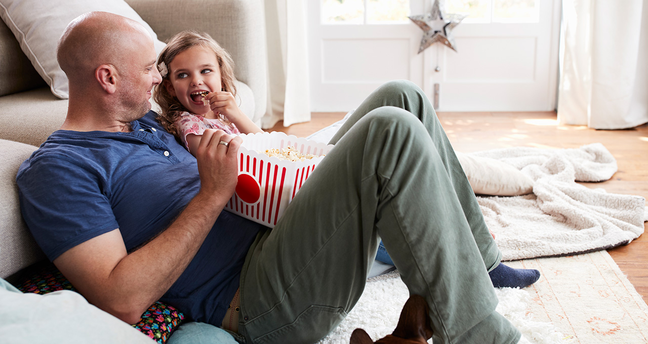 A parent and child sharing popcorn while watching a movie