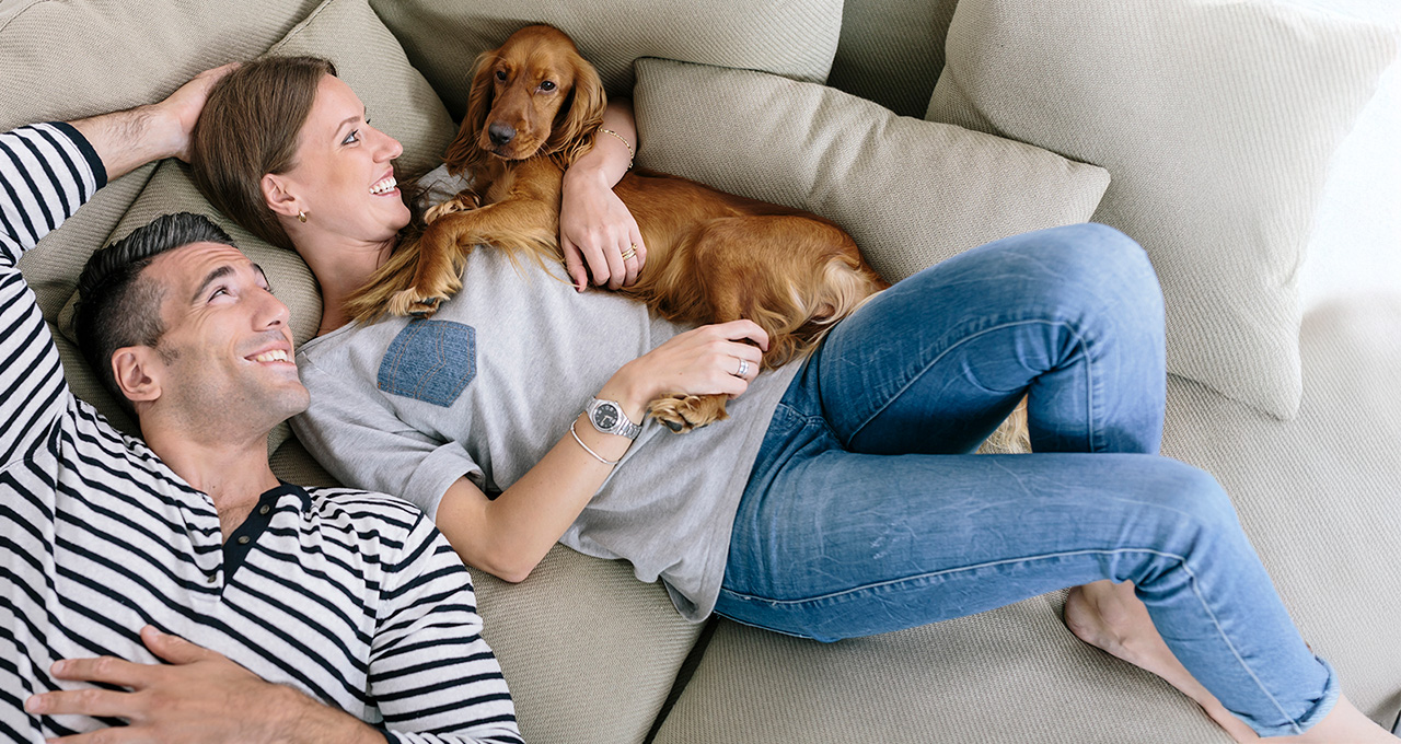 A couple relaxing on a sofa with a dog on their lap