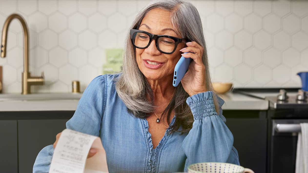 An older person talking on her cell phone while looking at a receipt.