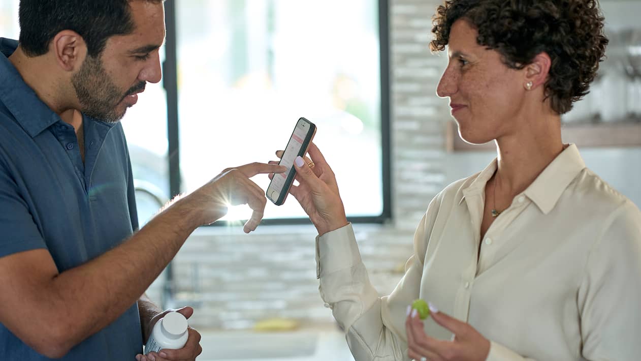 A person pointing to a cell phone screen held by their partner.